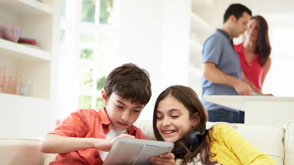 Frère et soeur jouant sur tablette tandis que les parents préparent le diner