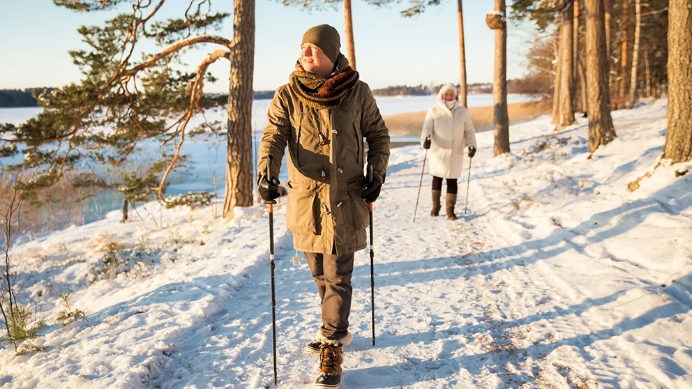 Un couple âgé marche sur un sentier enneigé près d’un lac.