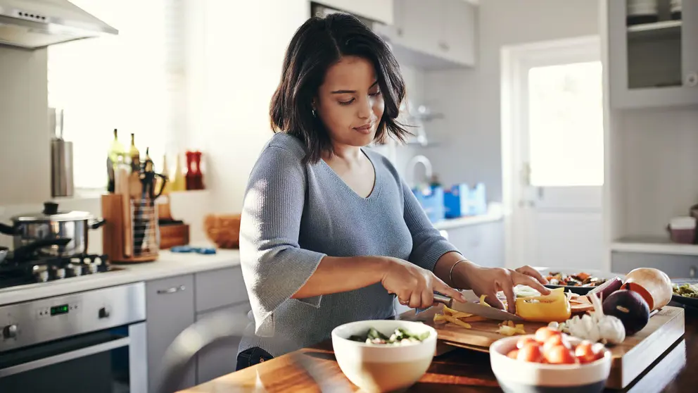 Une femme coupe des légumes dans sa cuisine.