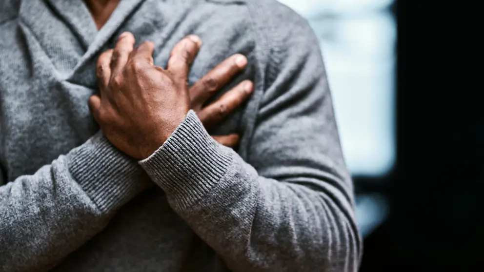 Un homme portant un chandail gris a les mains croisées sur son cœur.