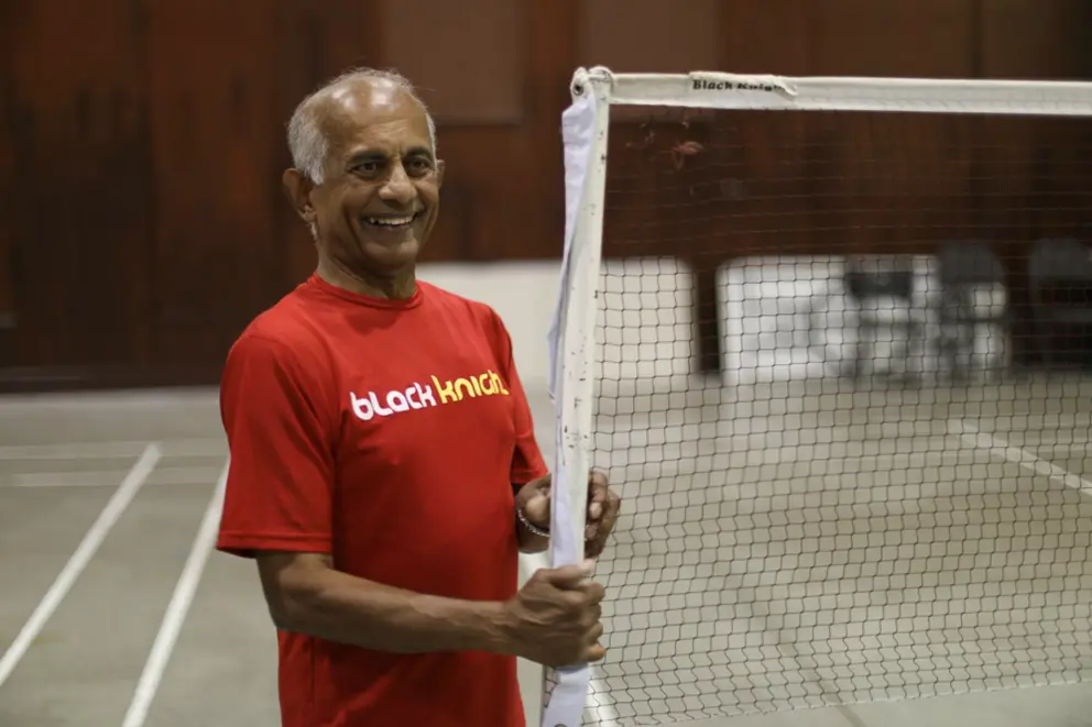 Jerry porte un t-shirt rouge à côté d’un filet de badminton dans un gymnase.