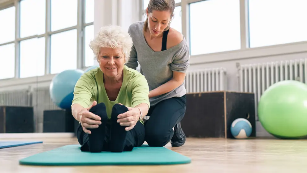 femme assise sur le plancher d'étirement des jambes avec un entraîneur personnel