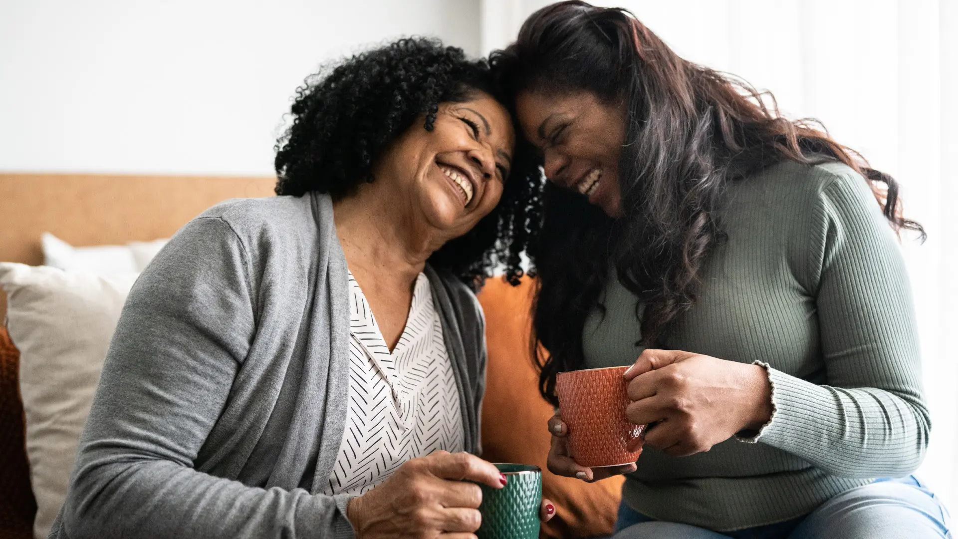 Deux femmes rient ensemble, tête contre tête et une tasse à la main.