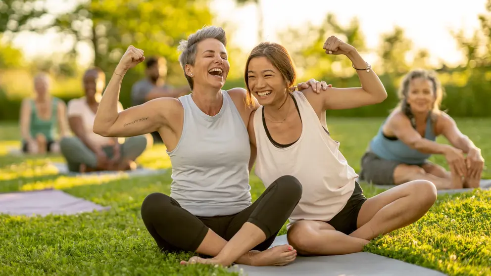 Deux femmes rient en se serrant et en montrant leurs biceps.