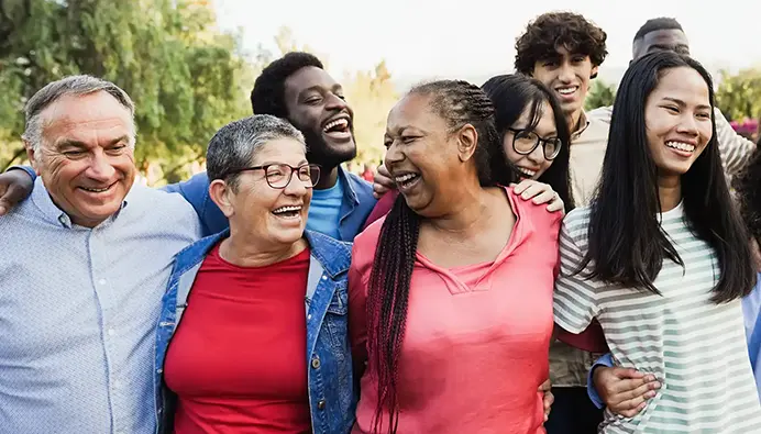 Un grand groupe diversifié de personnes s’enlacent à l’extérieur en souriant.